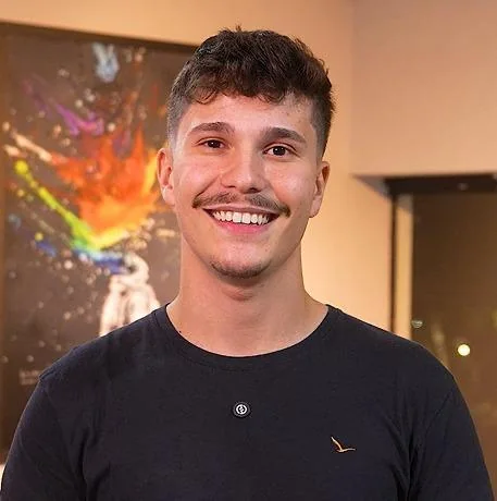Teacher Lucas sorrindo, de camiseta preta, em frente a um quadro colorido